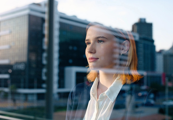 businessperson staring out a window with office building reflections