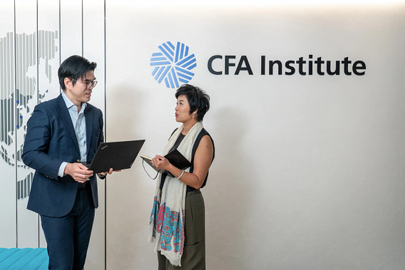 Two colleagues stood talking in front of the CFA Institute logo with their laptops in their hands