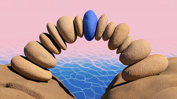 A striking arrangement of smooth, rounded stones forms an arch over a shimmering body of water. The stones are predominantly beige, with one blue stone strategically placed in the center of the arch, creating a focal point.