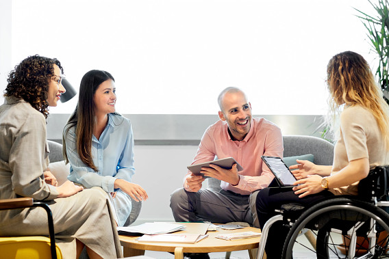 Smiling coworkers listening to a wheelchair user leading a discussion