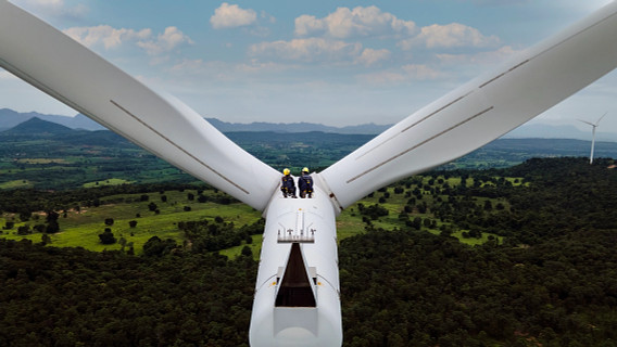 a close shot of two people crouched on the top of a wind turbine taken, from a drone